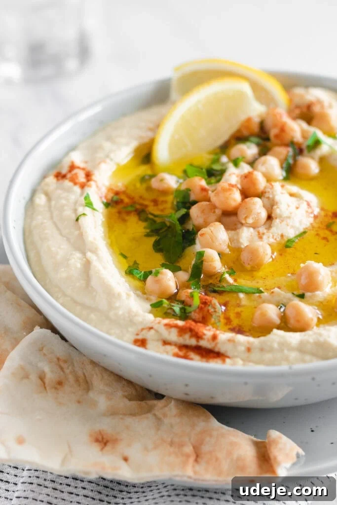 Velvety Authentic Hummus 2 A beautifully presented bowl of creamy homemade hummus, garnished with whole chickpeas, fresh parsley, a drizzle of olive oil, and a wedge of lemon, inviting a delightful culinary experience.