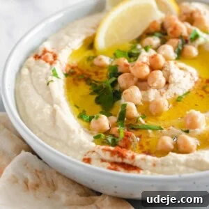 Velvety Authentic Hummus 3 Creamy hummus served in a bowl and garnished with chickpeas, parsley and lemon wedges