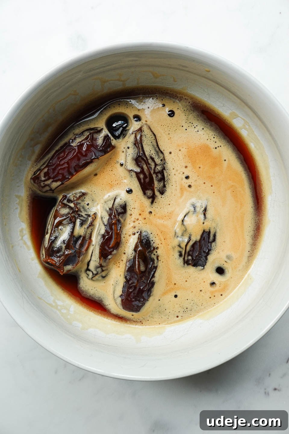 Tiramisu Date Delights 4 Large Medjool dates submerging in a bowl of dark black coffee, soaking up the rich flavor, a vital step for our unique tiramisu dessert.