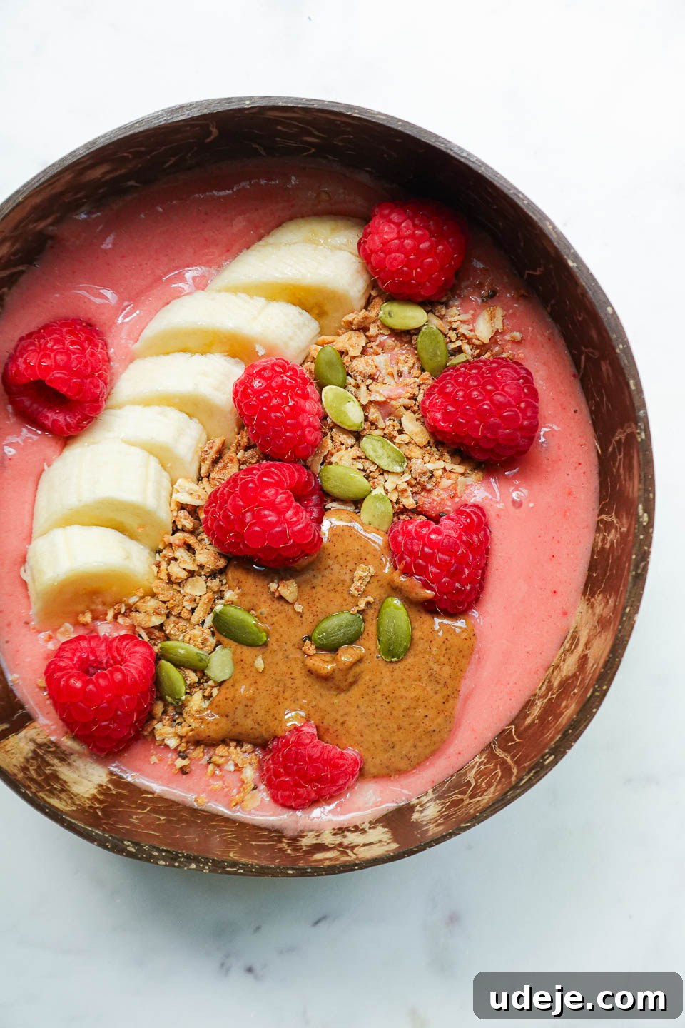 Simple and Delicious Vegan Raspberry Smoothie Bowl 5 Close-up of raspberry smoothie bowl topped with granola, sliced banana, fresh raspberries, almond butter, pumpkin seeds