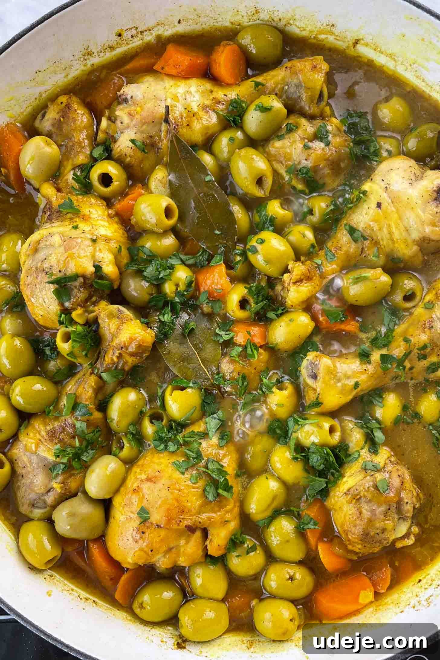 Chicken and Green Olive Tagine 11 A chicken and olive stew with carrots and a rich brown broth in a white pan, garnished with fresh chopped parsley on a marble background, ready to be served.