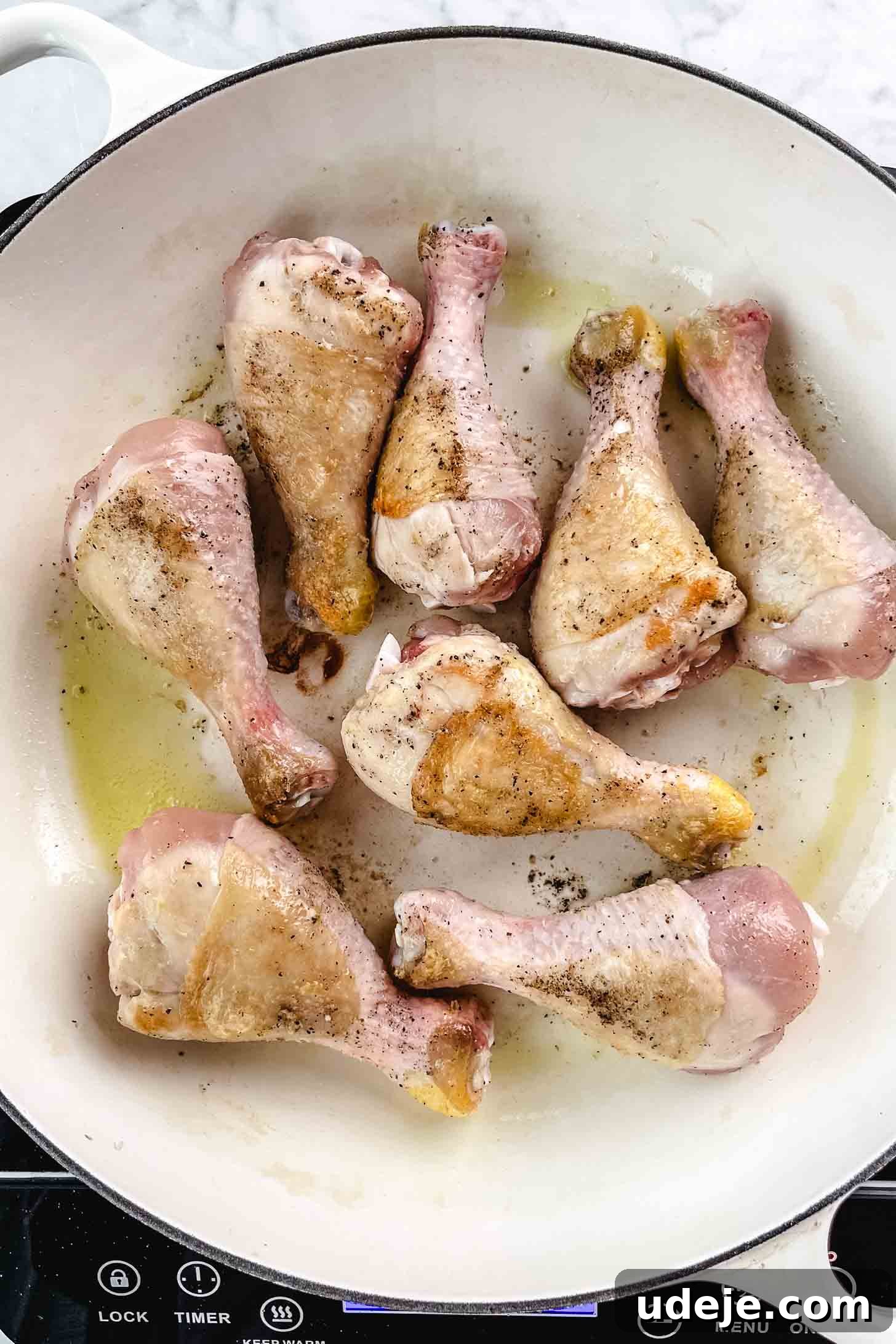 Chicken and Green Olive Tagine 5 Perfectly browned chicken legs in a large white pan, seasoned with salt and pepper, after being fried in olive oil on a marble background, ready to be set aside for the next step of the Tajine.