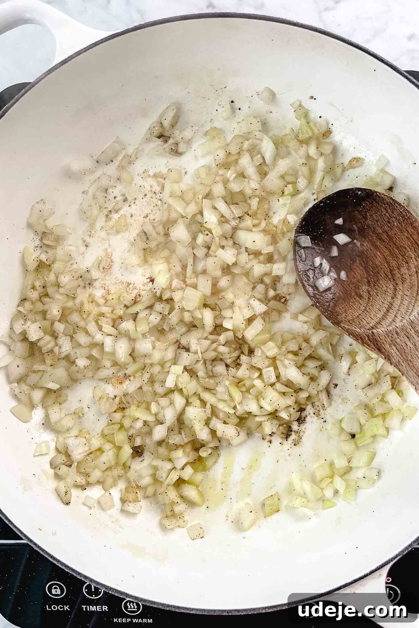 Chicken and Green Olive Tagine 6 Finely chopped onions being sautéed in a large white pan on a marble background, transforming into a sweet, translucent base for the stew.