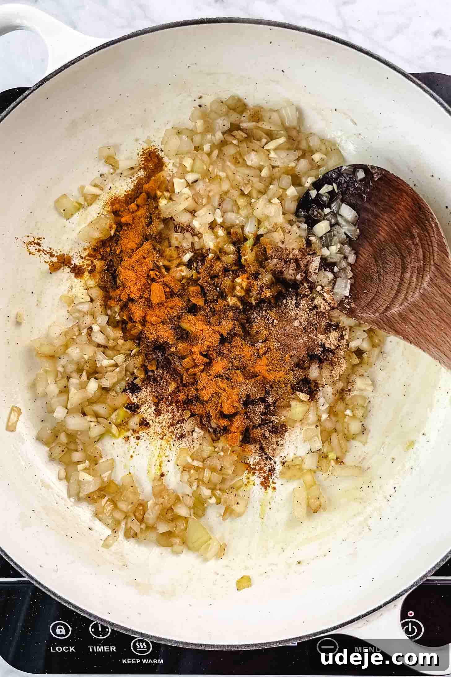 Chicken and Green Olive Tagine 7 Sautéed chopped onions in a large white pan with a vibrant blend of North African spices on top, being stirred with a wooden spoon on a white marble background, releasing their aromatic flavors.