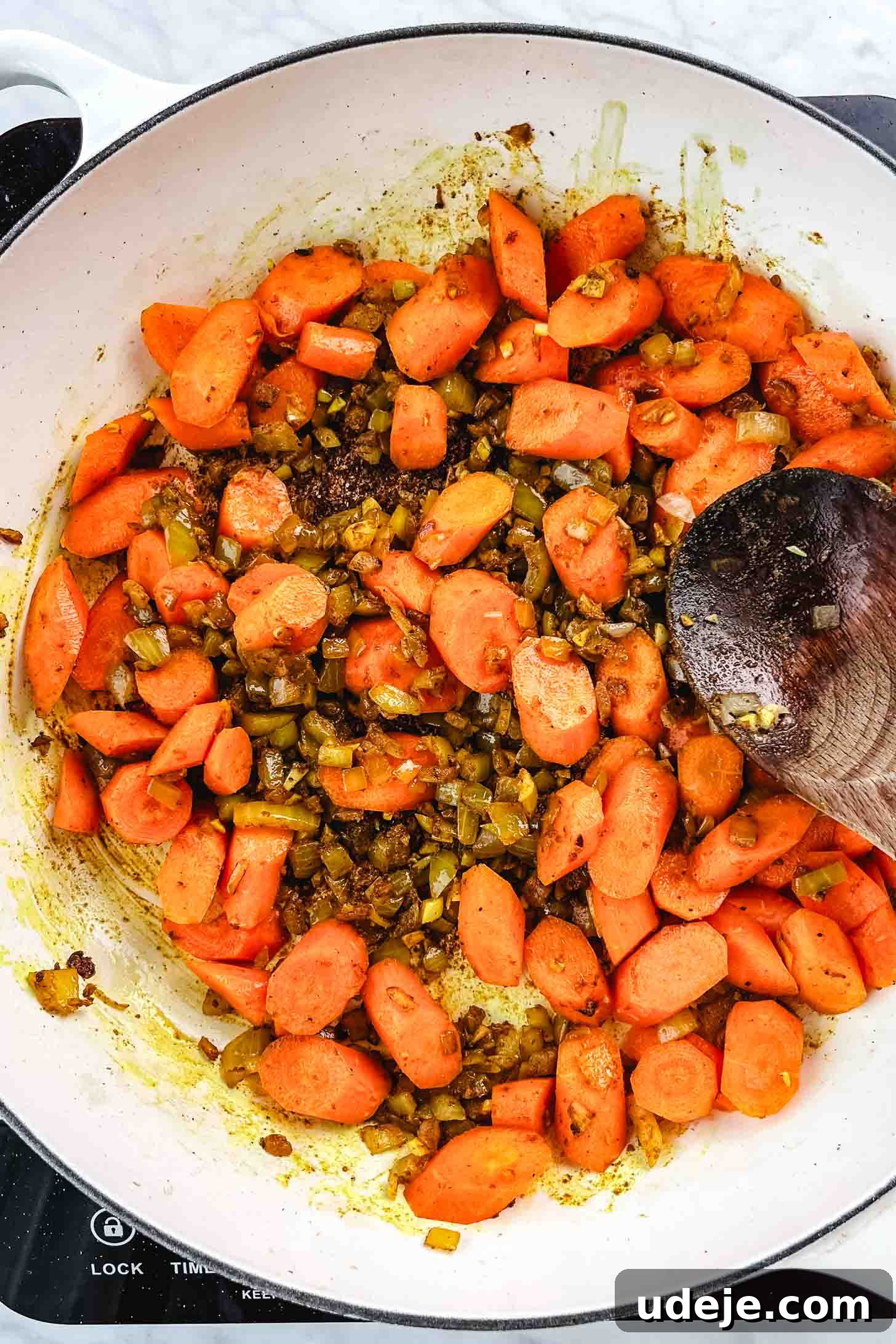 Chicken and Green Olive Tagine 8 Sautéed chopped onions mixed with spices, topped with sliced carrots, being stirred with a wooden spoon in a large white pan on a white marble background, preparing for the next stage of simmering.