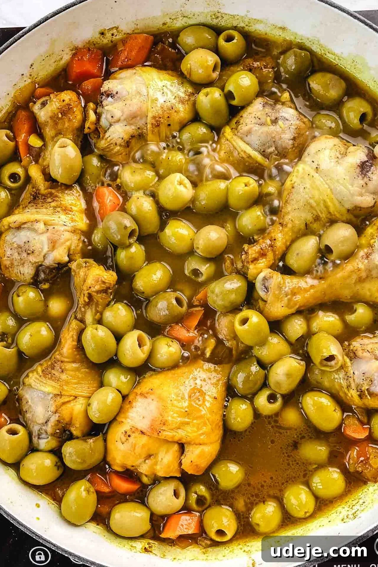 Chicken and Green Olive Tagine 10 Sliced carrots, whole green olives, and chicken legs submerged in a flavorful brown broth, simmering in a white pan on a marble background, creating a hearty and aromatic stew.