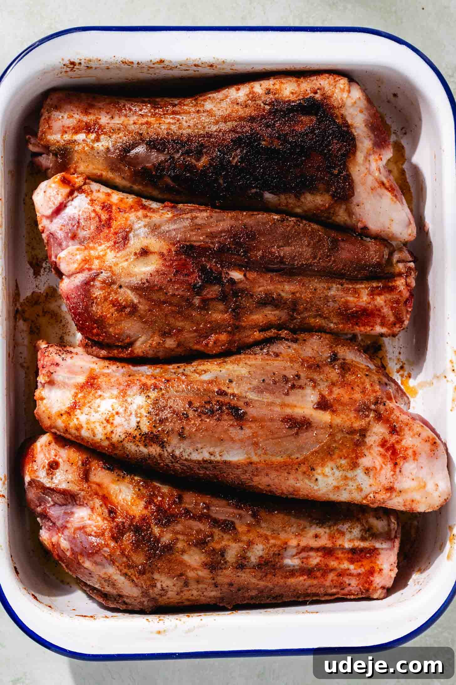 Melt-in-Your-Mouth Oven Braised Lamb Shanks 5 Four lamb shanks beautifully browned and seared on all sides, showcasing a rich crust from cooking, now resting in a white and blue rectangular dish after being removed from the pot.