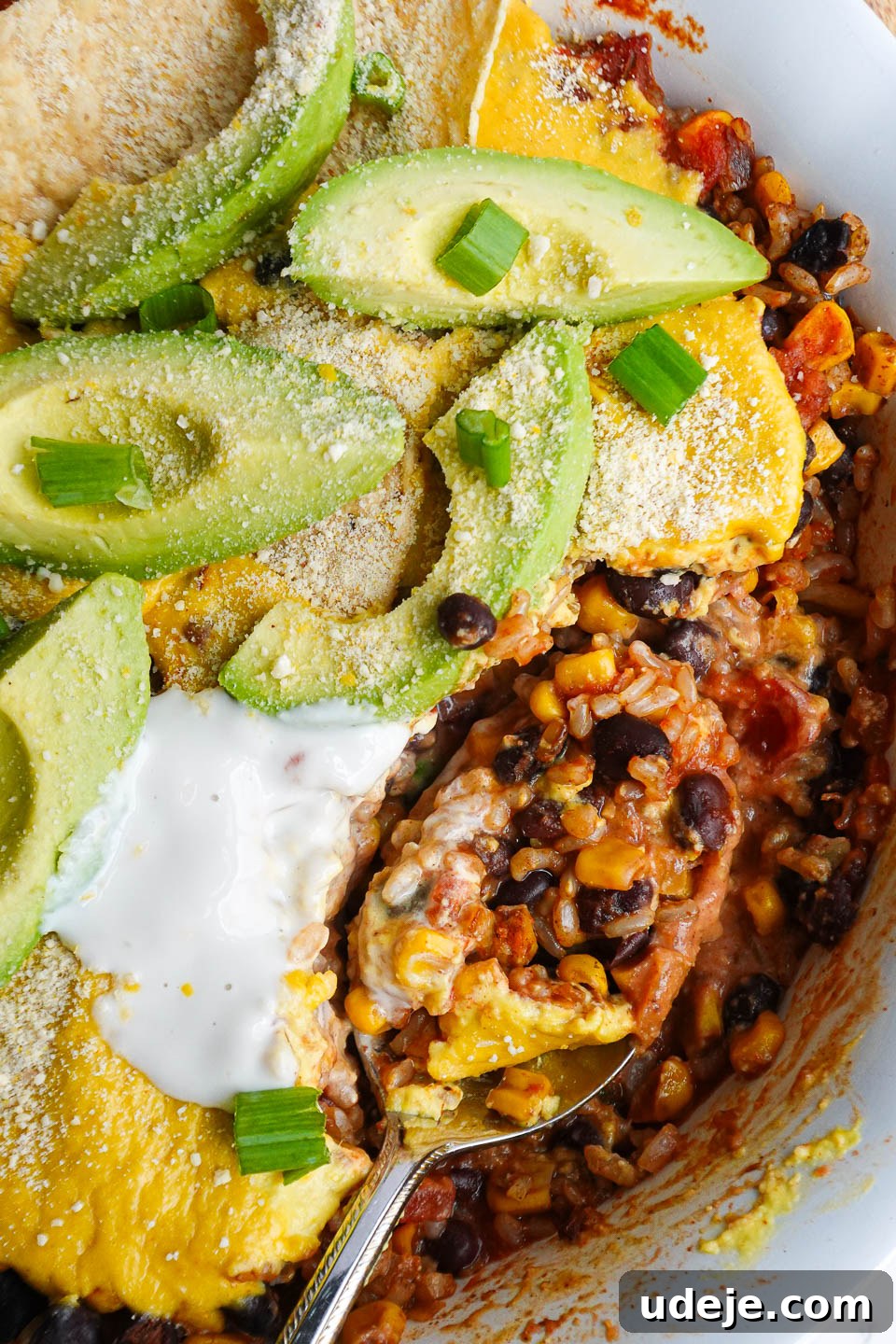 Plant Based Mexican Rice Bake 2 Close-up of a spoon scooping out casserole showing layers of rice, beans, corn, salsa, and creamy vegan queso