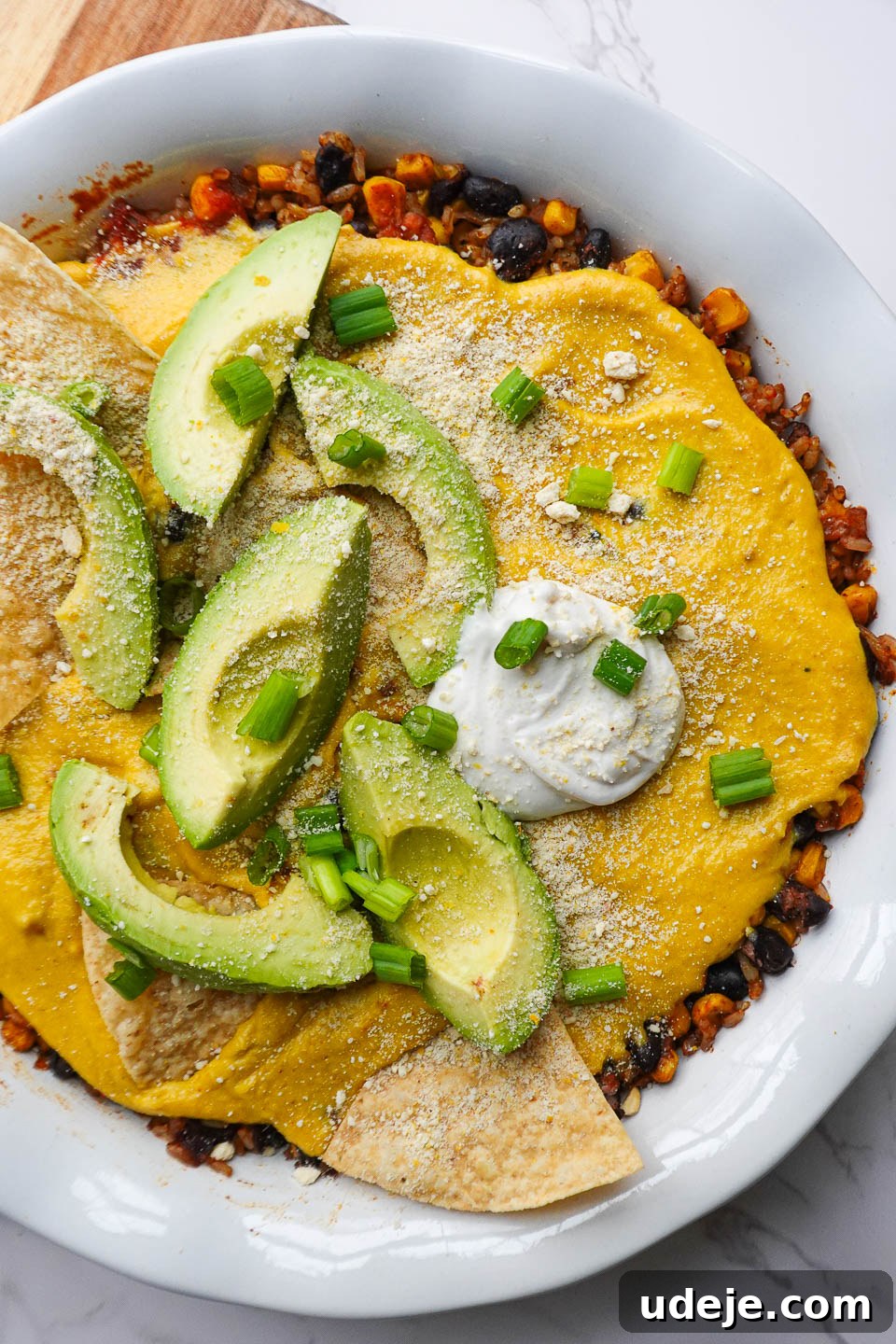 Plant Based Mexican Rice Bake 3 Overhead shot of vegan Mexican rice casserole in a baking dish topped with avocado slices, vegan sour cream, tortilla chips, and scallions