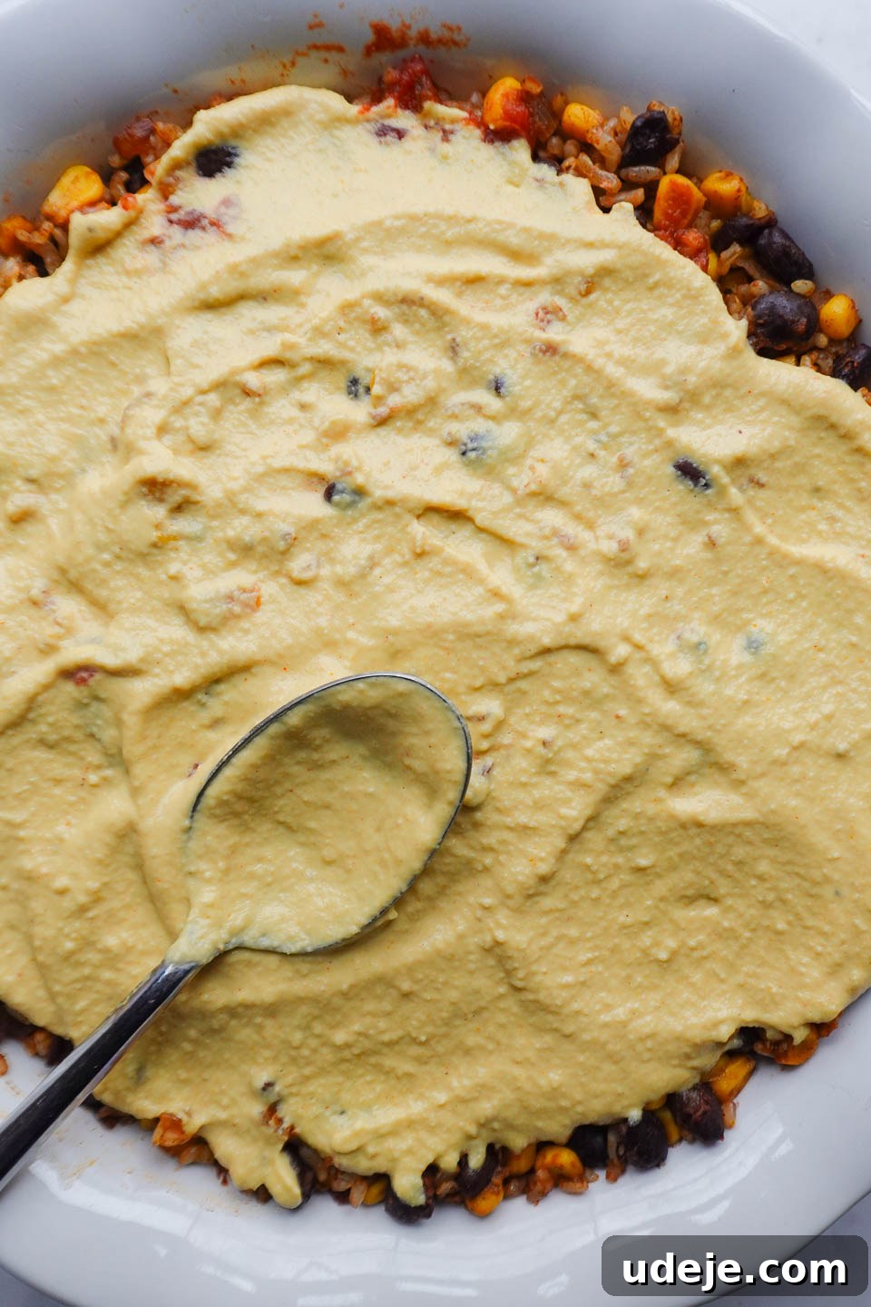 Plant Based Mexican Rice Bake 7 Vegan queso being poured over the assembled casserole
