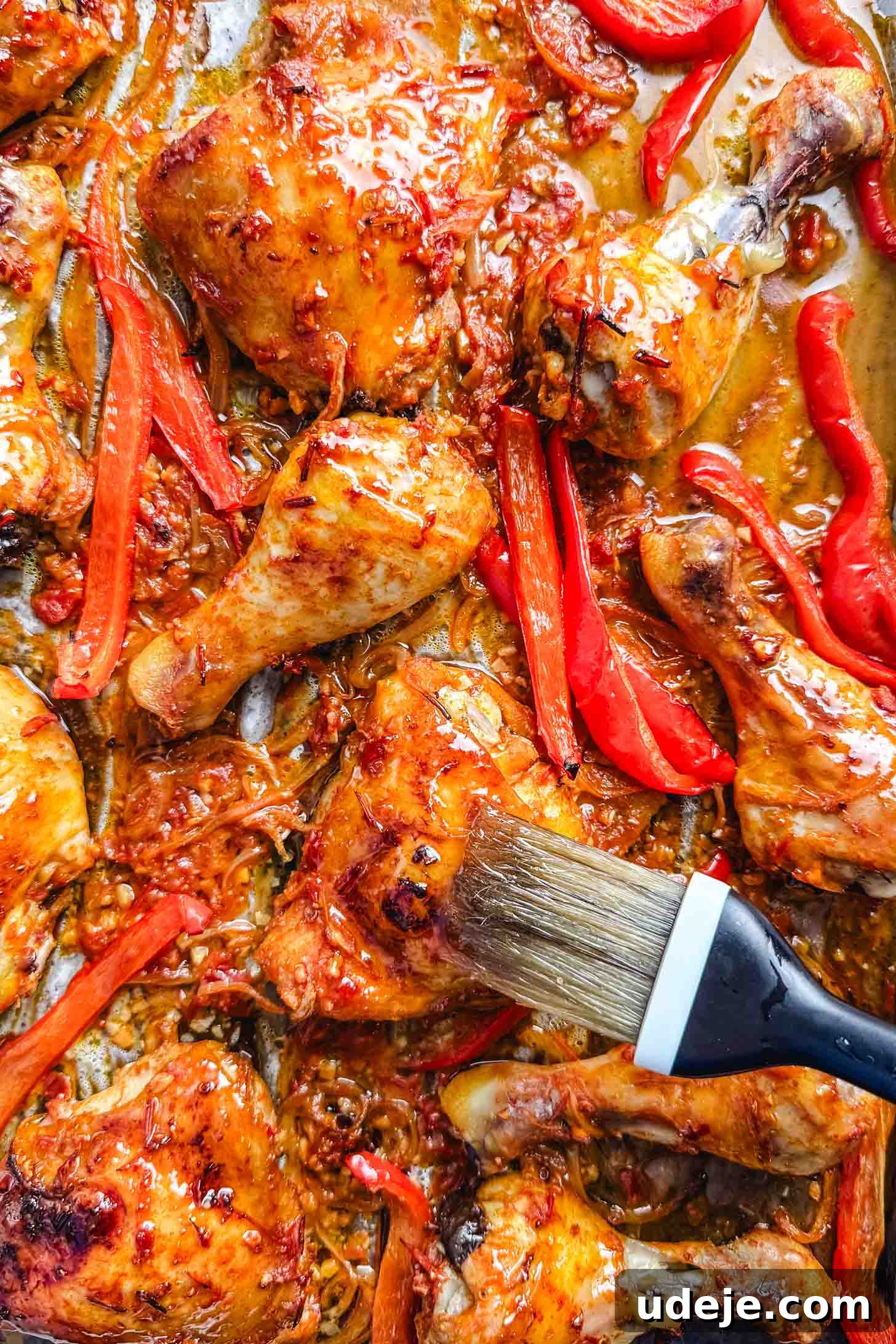 Sticky Harissa Honey Glazed Chicken 7 Baked red chicken legs and thighs and sliced red peppers with a pastry brush brushing one of the chicken thighs.