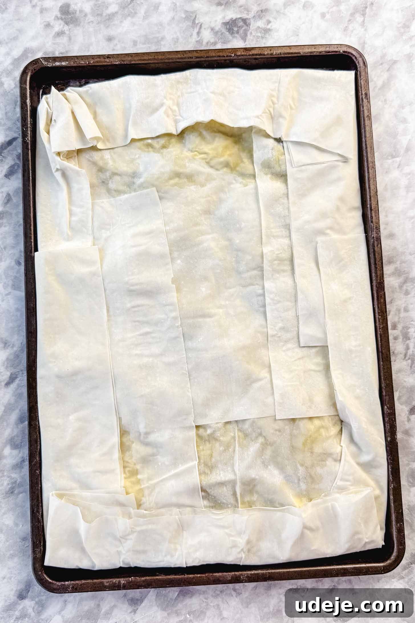 Easy Spinach Borek with Frozen Spinach and Phyllo 13 Folded over phyllo pastry in a sheet pan on a marble background. The borek is now sealed and ready for the final top layers.