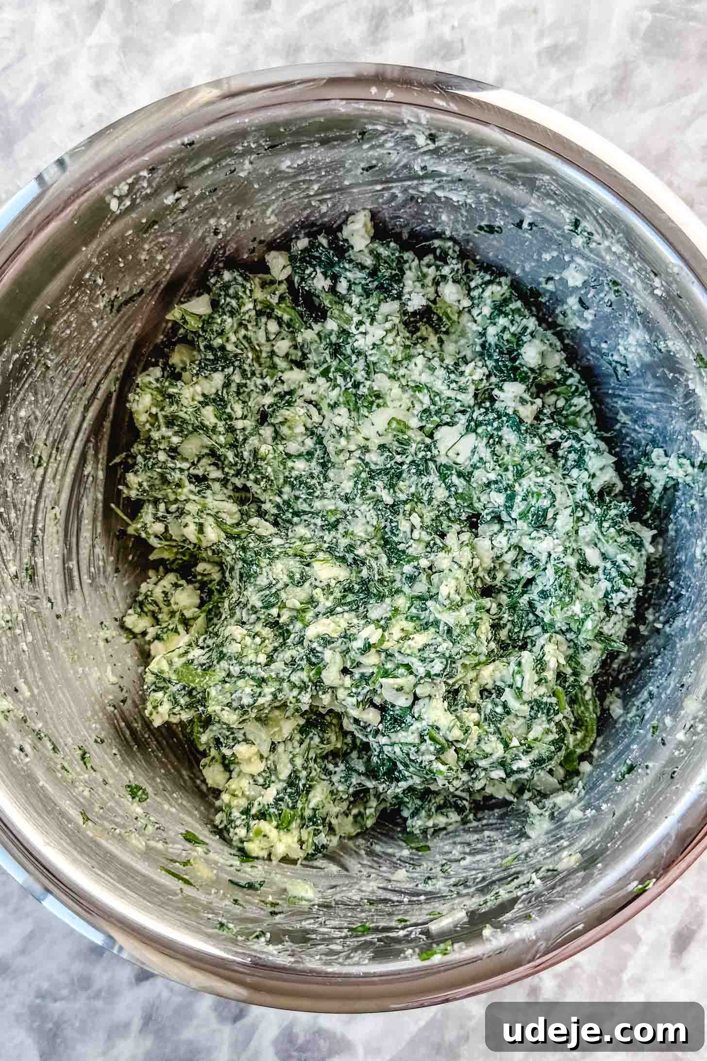 Easy Spinach Borek with Frozen Spinach and Phyllo 5 Spinach and cheese filling mixture in a metal bowl on a marble background. The mixture is well combined and ready for assembly.