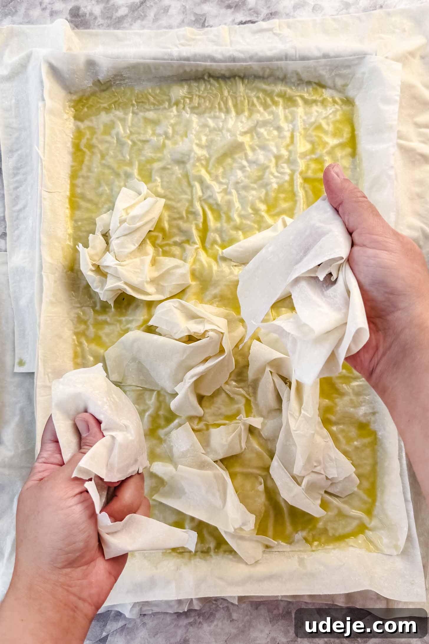 Easy Spinach Borek with Frozen Spinach and Phyllo 8 Phyllo pastry brushed with butter and olive oil on top of the sheet pan with phyllo pastry being scrunched up and placed on top on a marble background. This shows the technique for creating air pockets.