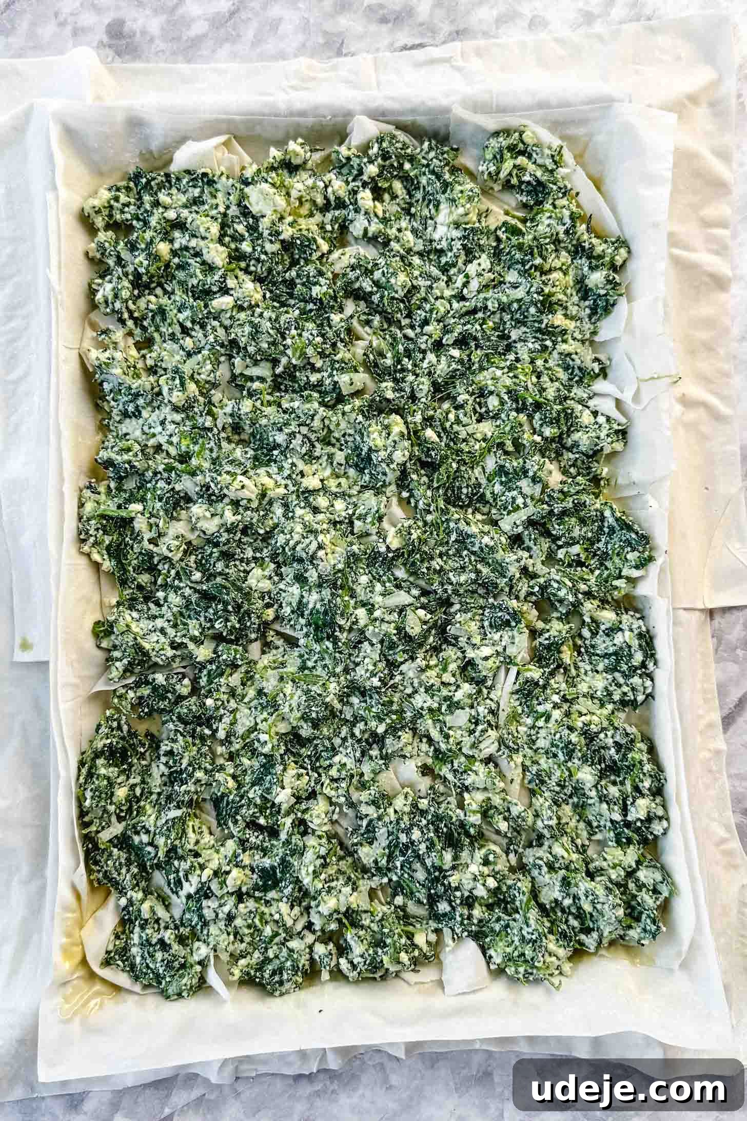 Easy Spinach Borek with Frozen Spinach and Phyllo 10 Phyllo pastry in a sheet pan with a spinach and cheese mixture spread on top on a marble background. The borek is halfway assembled.