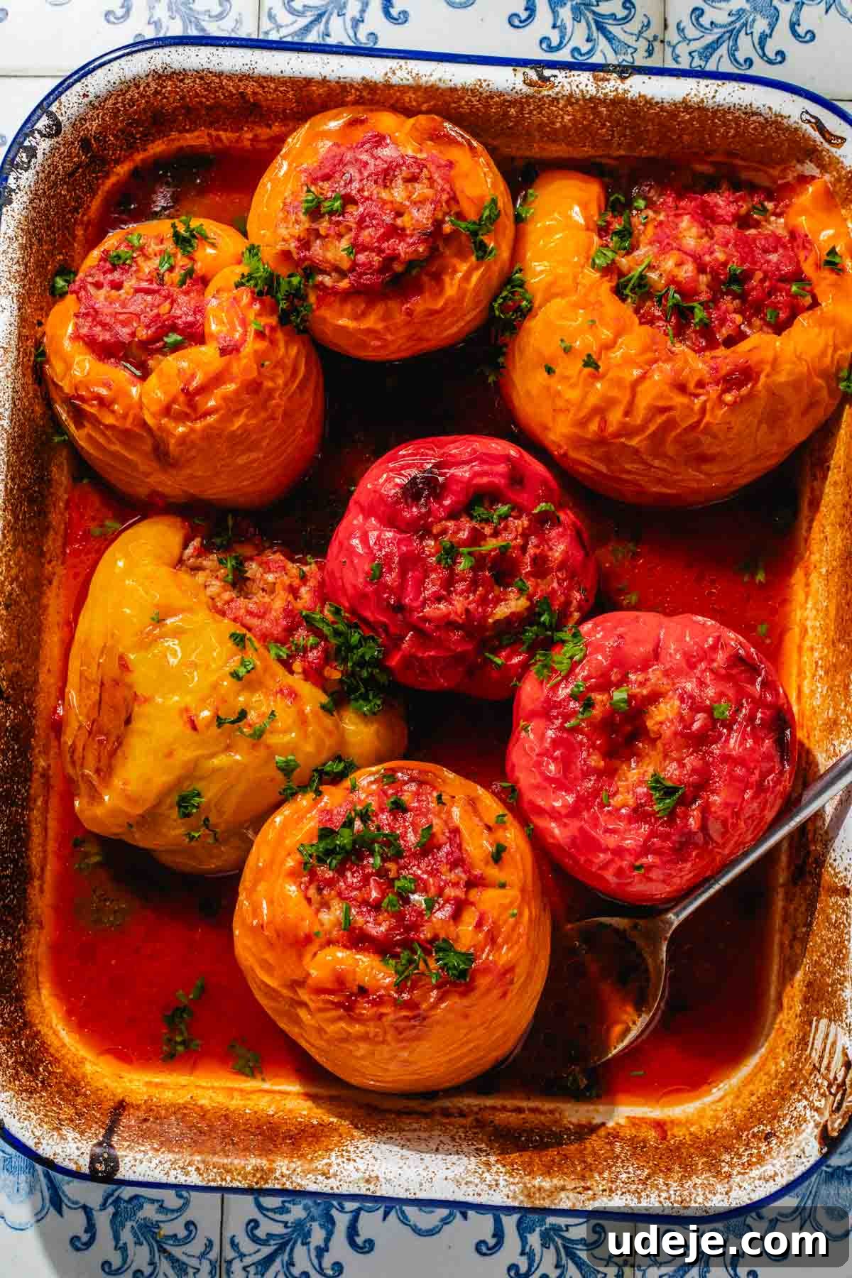 Mediterranean Veggie Stuffed Peppers 11 Baked yellow, orange and red bell peppers, stuffed with a rice mixture, placed in a large enamel baking dish with tomato sauce on the bottom, garnished with finely chopped parsley. The finished dish, ready to be enjoyed.