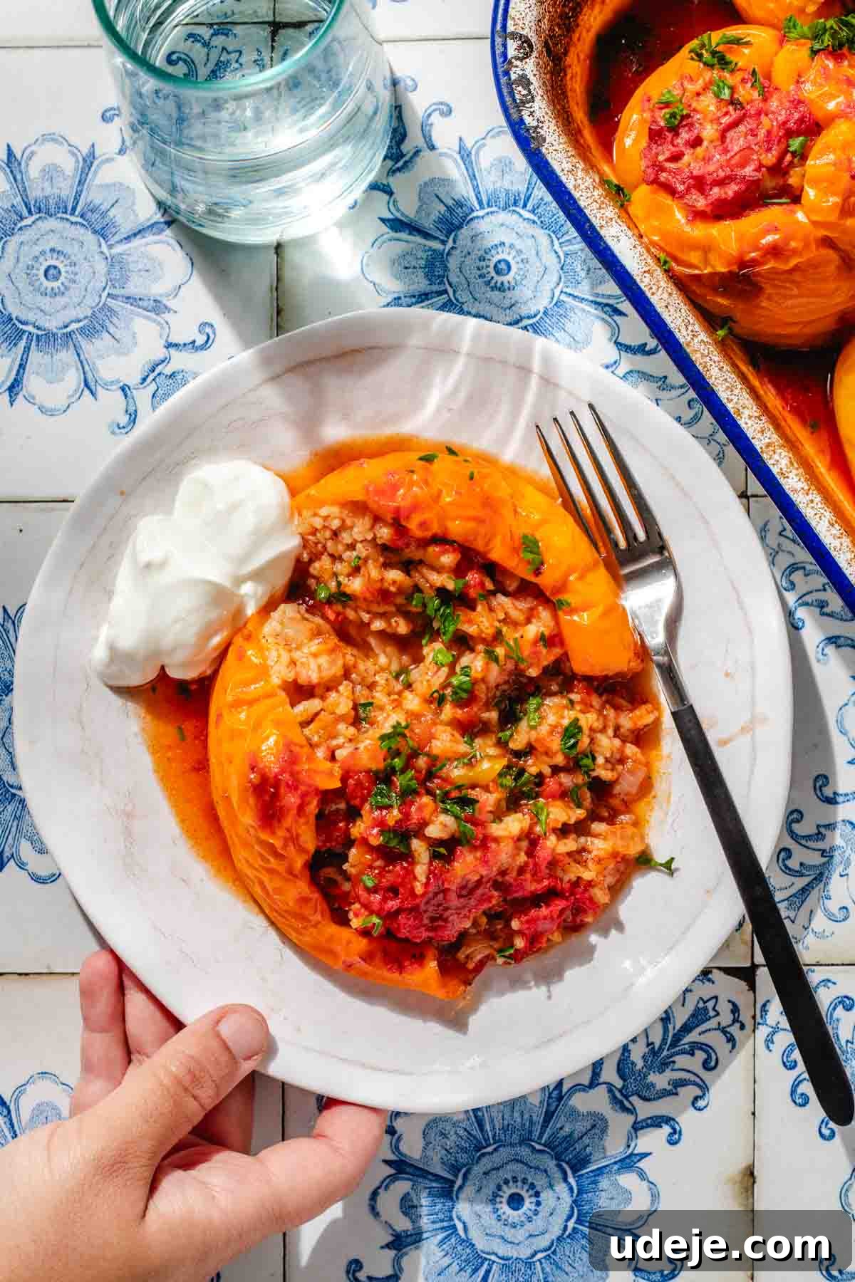 Mediterranean Veggie Stuffed Peppers 12 A large yellow bell pepper, stuffed with a rice mixture and baked, served on a small white plate with a fork and a dollop of yogurt.