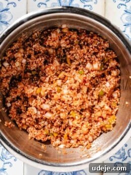 A raw rice stuffing which includes rice, chopped onions and peppers, tomato paste and spices, in a large stainless steel bowl