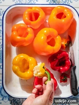 Large yellow, orange and red bell peppers that are hollowed out using a knife, placed in a large enamel baking pan.
