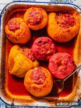 Baked yellow, orange and red bell peppers, stuffed with a rice mixture, placed in a large enamel baking dish with tomato sauce on the bottom.