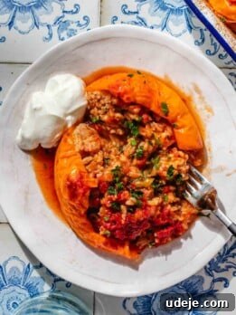 A large yellow bell pepper, stuffed with a rice mixture and baked, served on a small white plate with a fork and a dollop of yogurt.