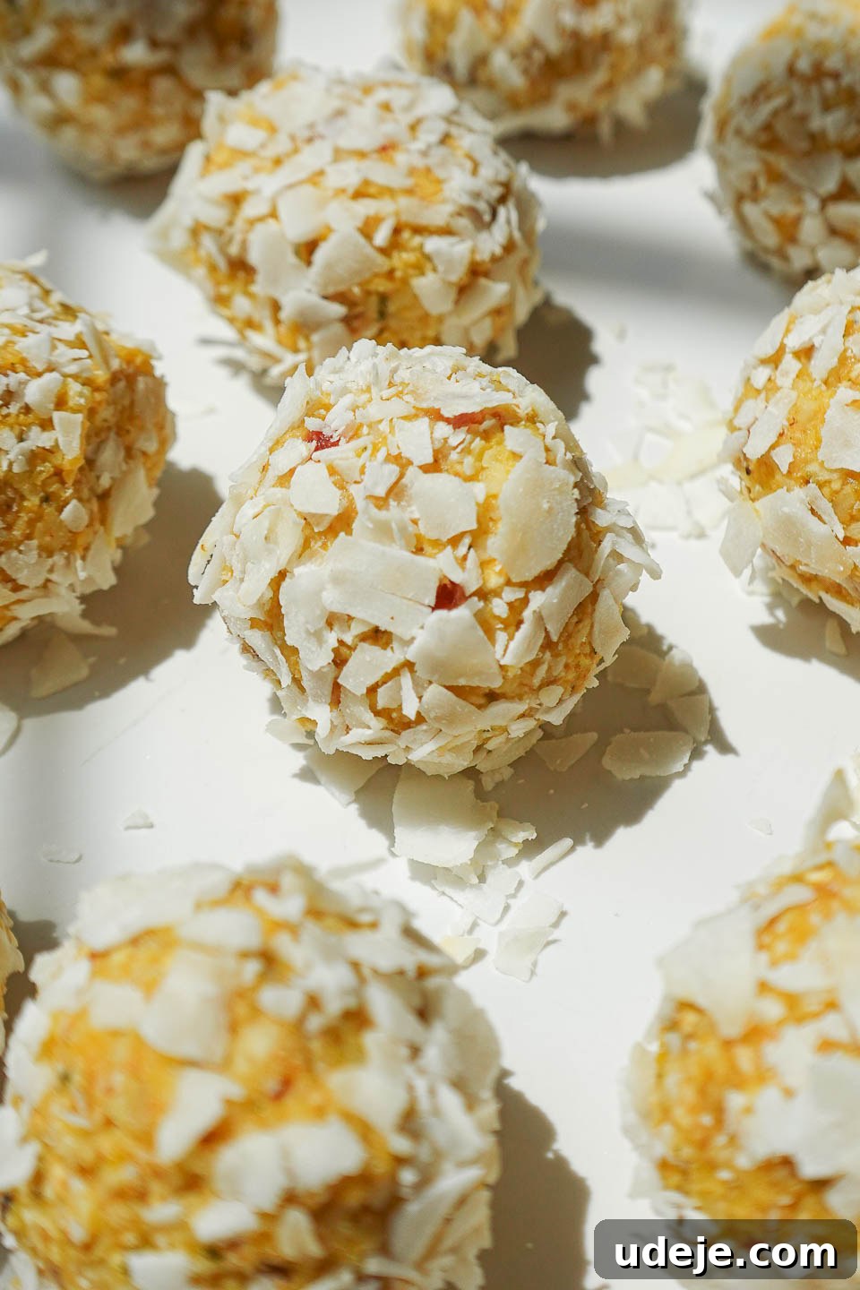 Vegan No-Bake Mango Energy Bites 4 A plate of no-bake mango bliss balls rolled in shredded coconut, arranged on a white plate, ready to be eaten.