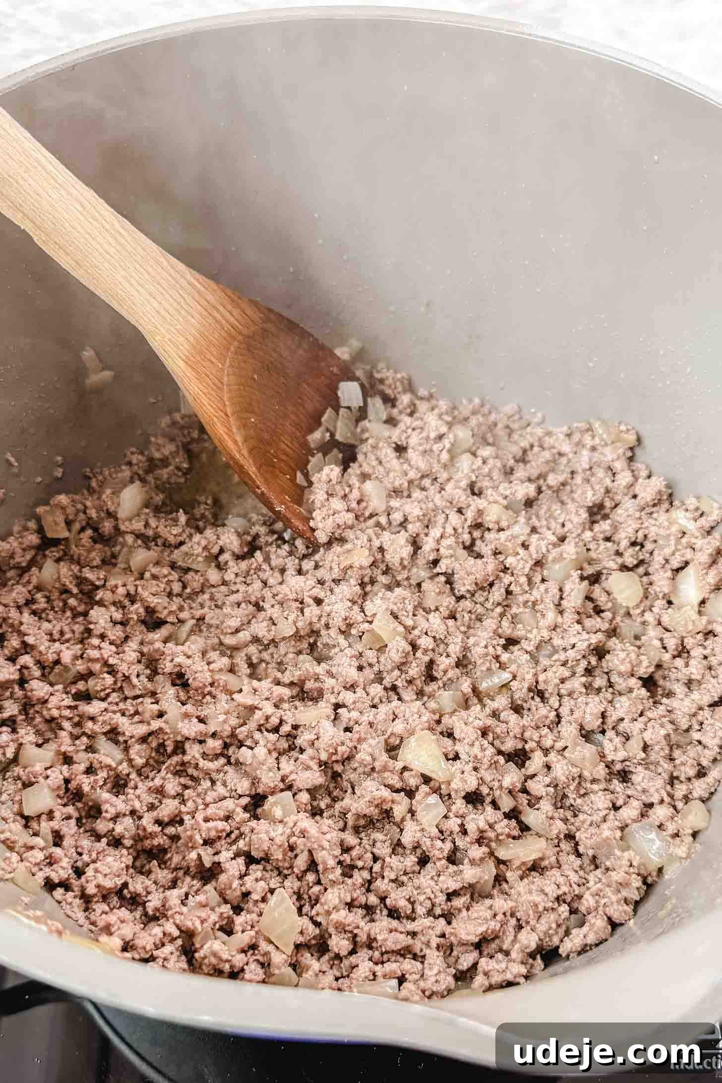 Authentic Afghan Aush Hearty Noodle Delight 4 Ground beef with finely chopped onions gently cooking in a cream-colored soup pot, stirred with a wooden spoon on a pristine marble background.