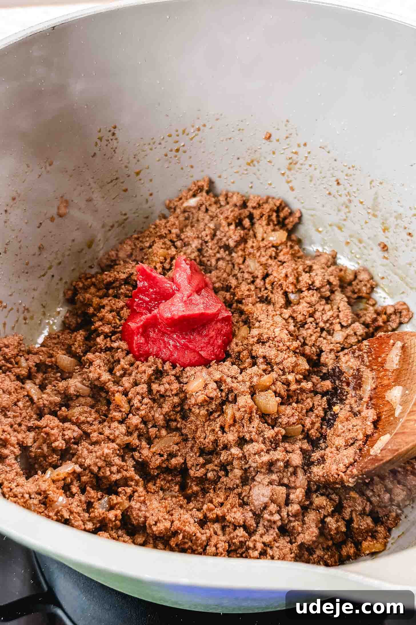 Authentic Afghan Aush Hearty Noodle Delight 6 Sautéed and seasoned ground beef expertly blended with rich tomato paste in a cream-colored pot, ready for the next stage of flavor development with a wooden spoon for mixing.