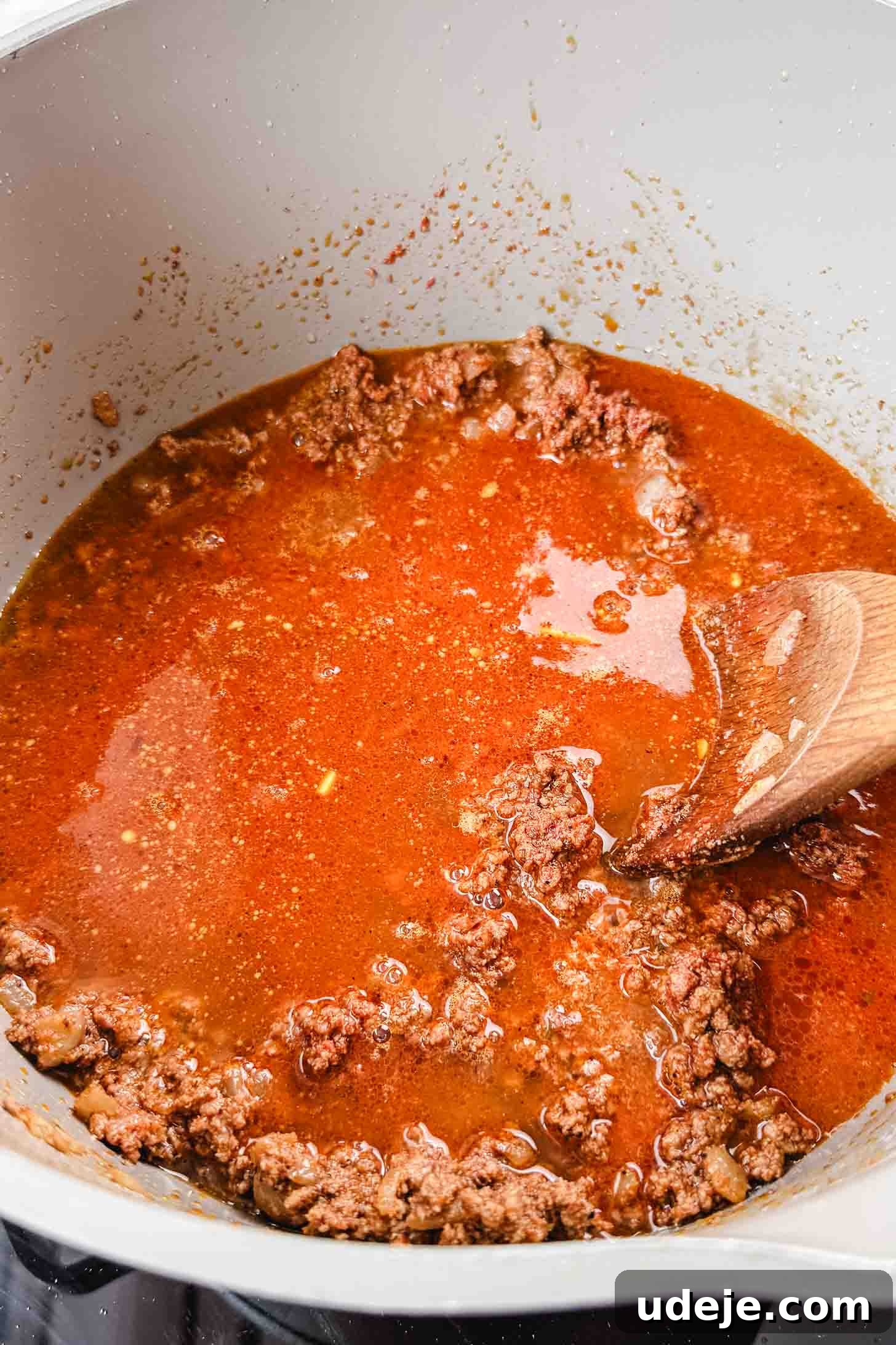 Authentic Afghan Aush Hearty Noodle Delight 7 Richly cooked and seasoned ground beef, vibrant with tomato paste and a ladle of broth, simmering in a cream-colored pot, stirred with a wooden spoon to blend the deep flavors for a hearty soup base.