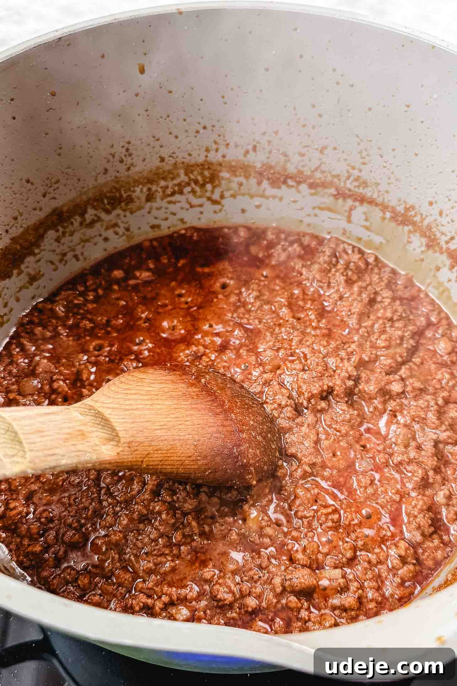 Authentic Afghan Aush Hearty Noodle Delight 8 Flavorful ground beef simmering in a rich stock within a cream-colored pot, a wooden spoon resting nearby on a marble background, illustrating the deep cooking process.