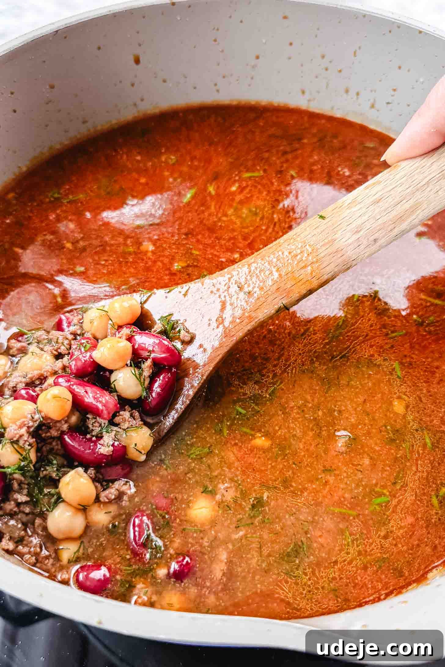 Authentic Afghan Aush Hearty Noodle Delight 10 Hearty Aush soup in a cream-colored pot with green handles, being scooped up with a wooden spoon, showcasing the rich broth, noodles, and beans on a marble background.