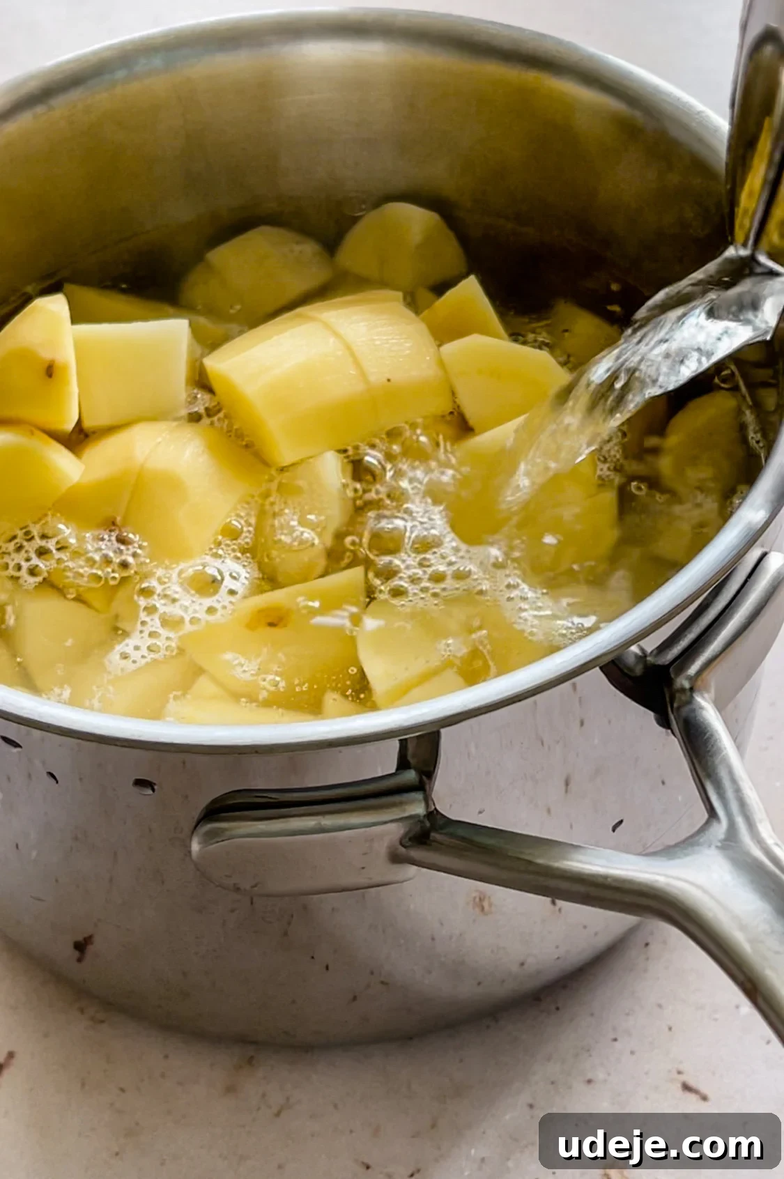 Spicy Golden Crispy Batata Harra 3 Cubed peeled potatoes in a medium stainless steel saucepan with water being poured inside