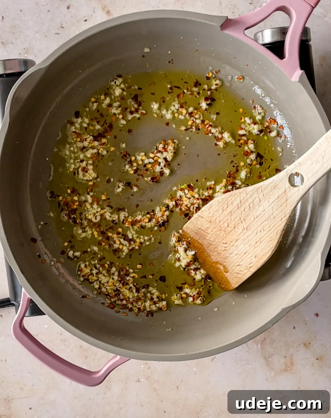 Spicy Golden Crispy Batata Harra 5 olive oil, garlic, and chili flakes in a skillet being cooked using a wooden spoon