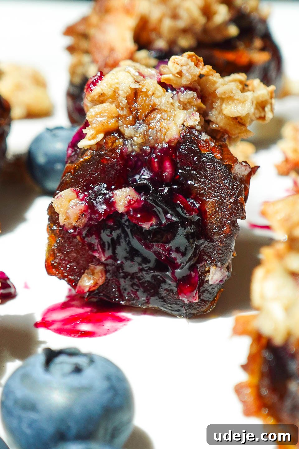 Blueberry Crisp Date Gems 5 Close-up of a Blueberry Crisp Stuffed Date with a bite taken out, showing gooey blueberry compote and perfectly golden oat topping