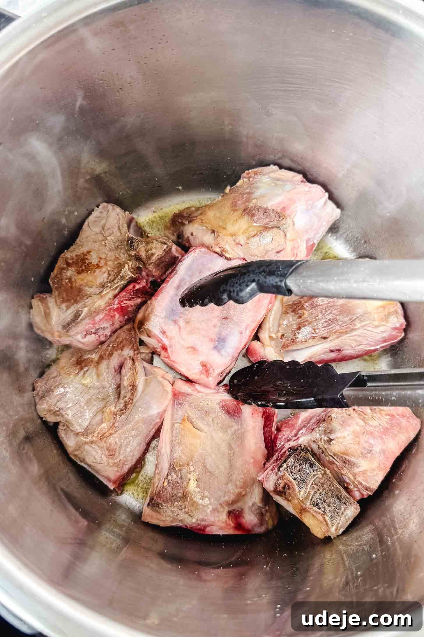 Mansaf: Jordan's Tangy Lamb Masterpiece 4 Lamb shoulder pieces being browned in a steel pot with black tipped tongs.
