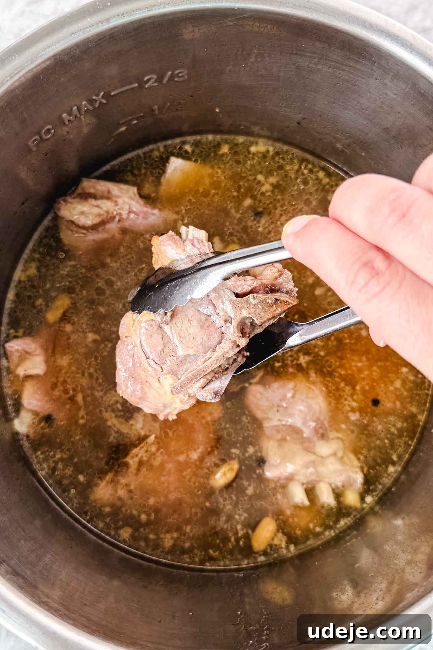 Mansaf: Jordan's Tangy Lamb Masterpiece 7 Cooked lamb shoulder being held over a steel pot with lamb and broth by tongs.