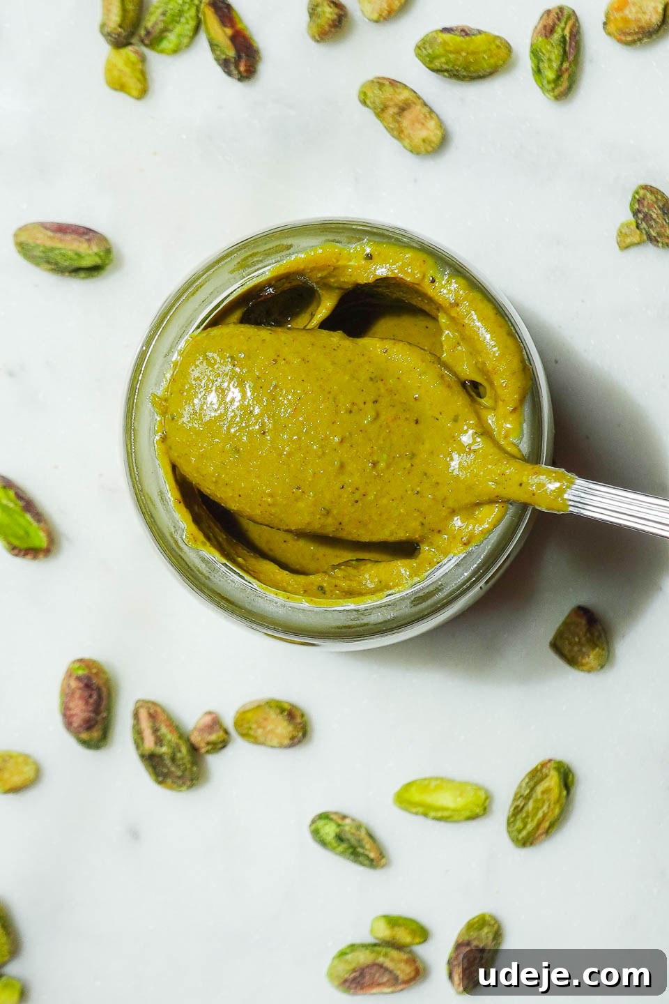 Artisan Pistachio Spread 2 Vibrant green homemade pistachio butter in a small glass jar on a elegant marble background, showcasing its smooth, spreadable texture.