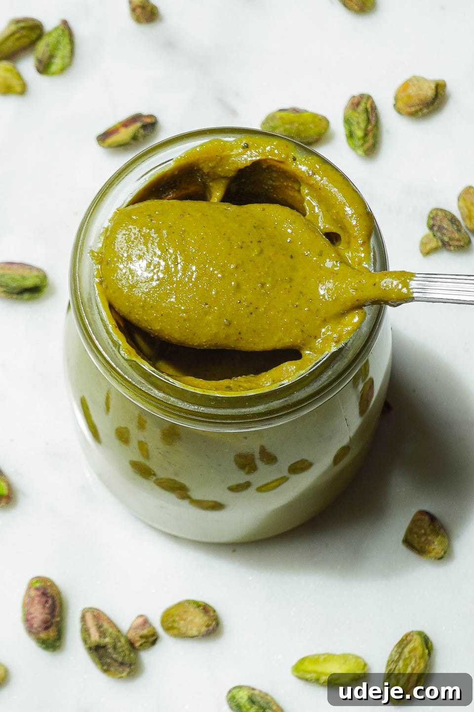 Artisan Pistachio Spread 11 A charming glass jar filled with luscious, creamy homemade pistachio butter, with a spoon resting invitingly beside it.
