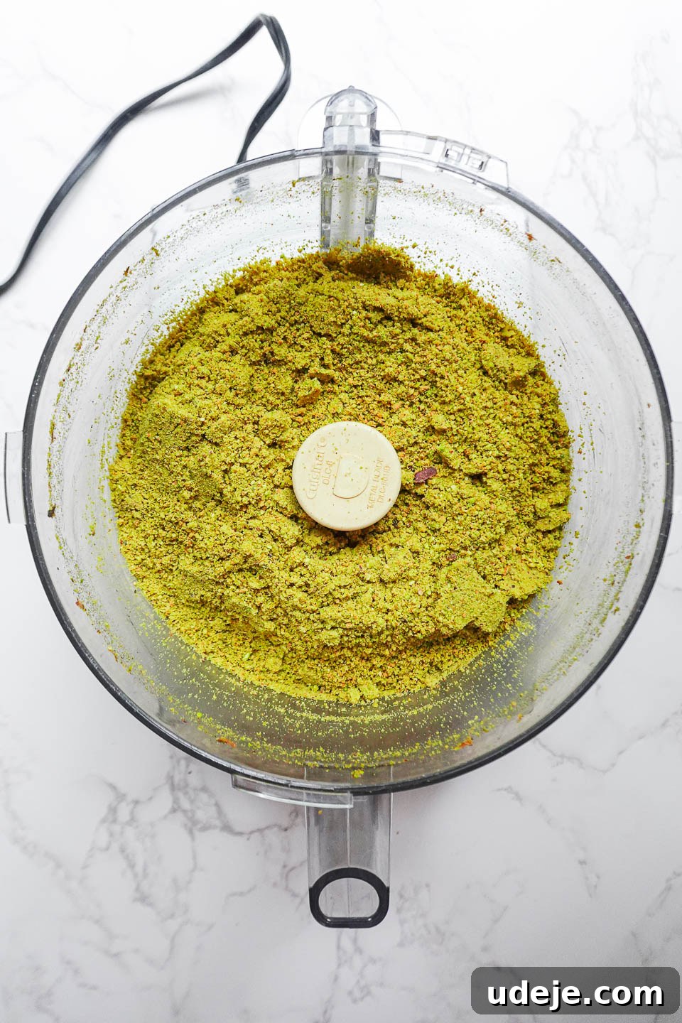 Artisan Pistachio Spread 8 Pistachios actively blending in a food processor, transitioning from a crumbly texture to a thicker, more dough-like consistency.