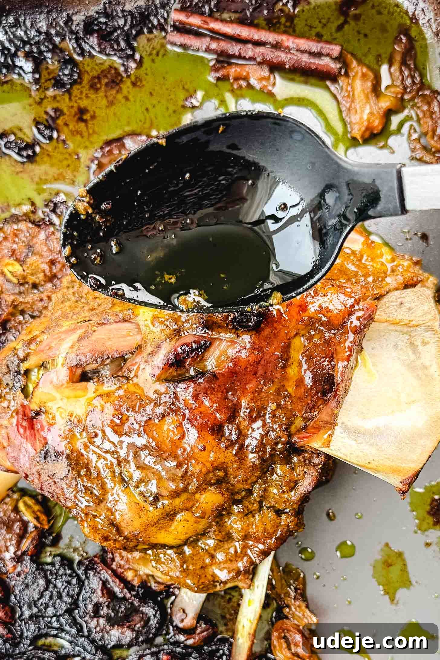 Fall-Apart Tender Lamb Haneeth 12 Roasted lamb shoulder in a large roasting pan with the juices being poured over it by a black spoon.