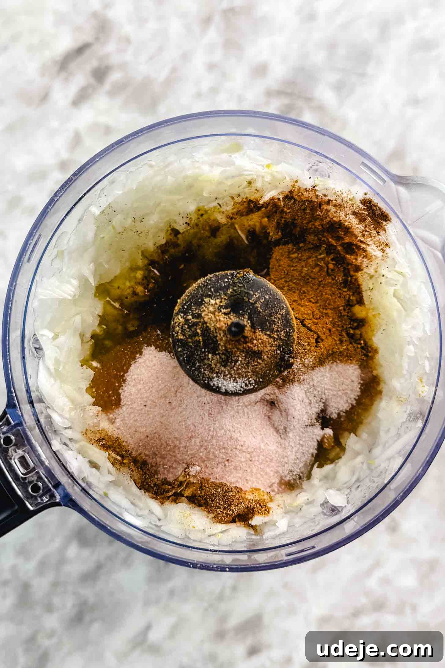 Fall-Apart Tender Lamb Haneeth 4 Small food processor with chopped onions and brown spices and pink salt on a marble background.