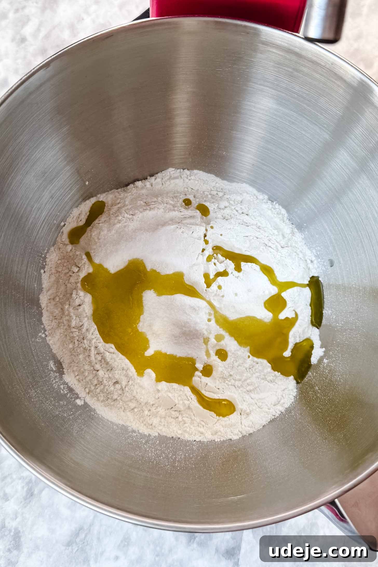 Customizable Homemade Turkish Pide 4 A large metal bowl containing flour, sugar, salt, and olive oil, resting on a pristine marble background, ready for dough preparation.