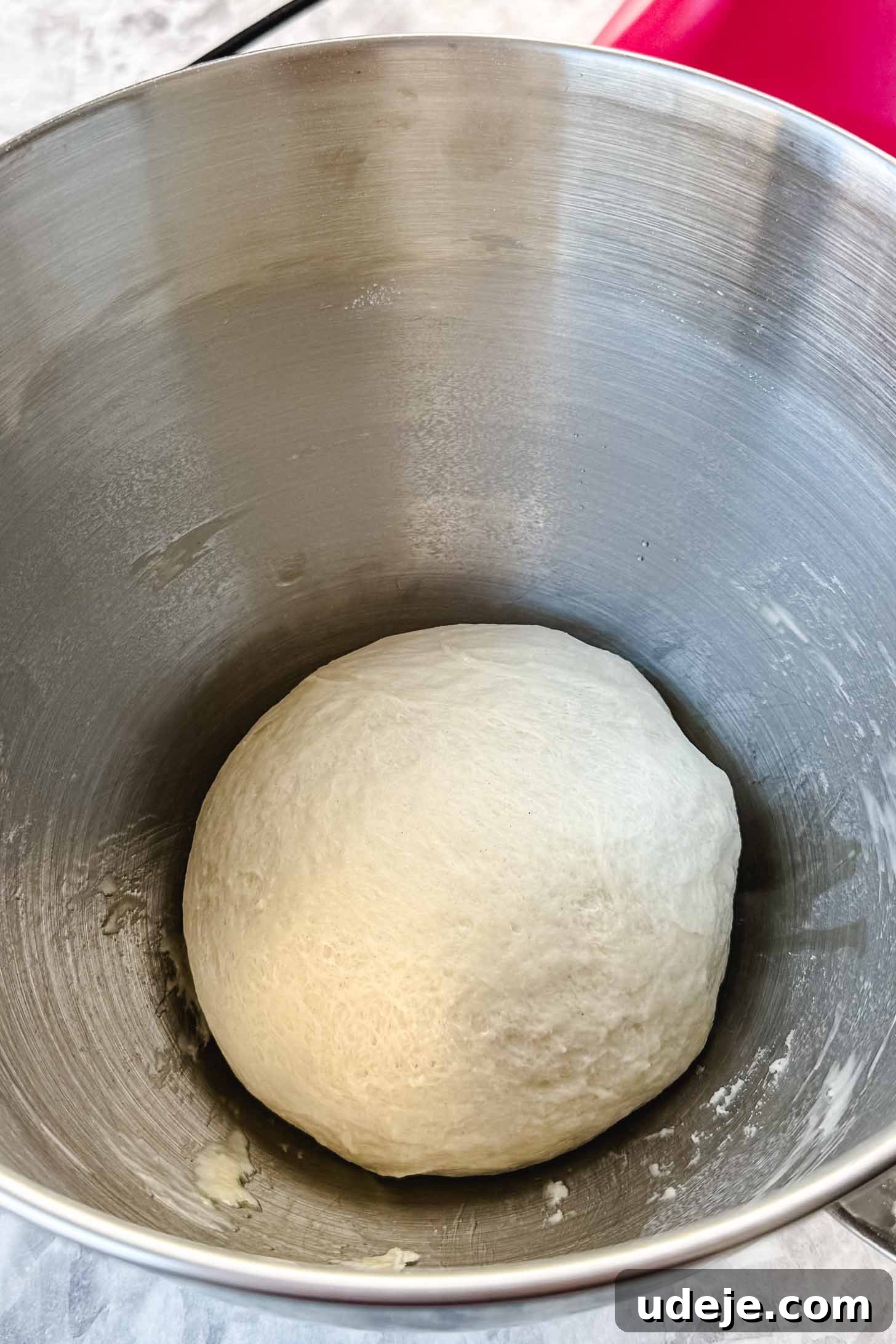 Customizable Homemade Turkish Pide 5 A perfectly kneaded, smooth dough ball nestled in a large metal bowl, set against a classic marble background, indicating it's ready for its first rise.