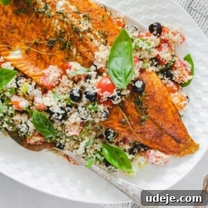 Rainbow trout fillet served over a bed of bulgur salad in a white plate, with a serving spoon and basil
