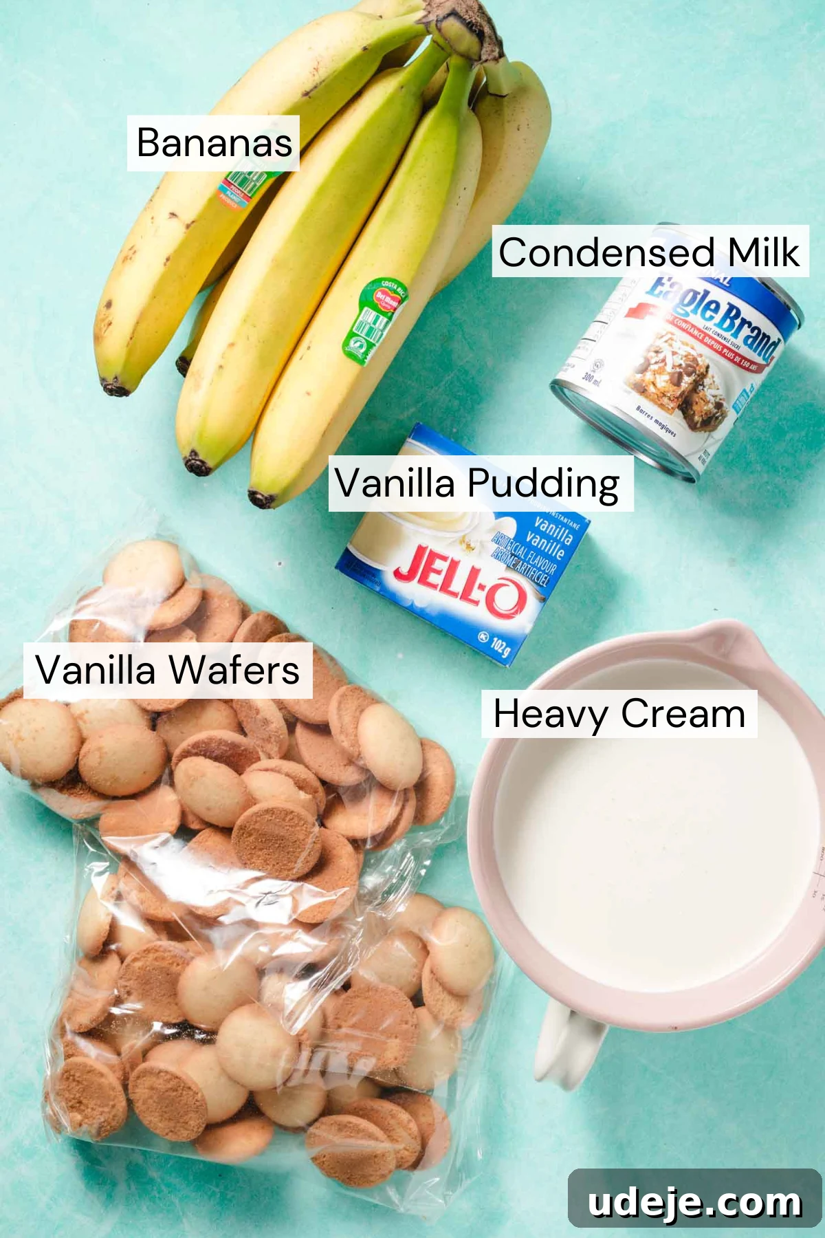 Magnolia Bakery's Irresistible Banana Pudding 3 Ingredient shot with a bunch of bananas, a can of condensed milk, a box of vanilla pudding, two packages of vanilla wafers, a white measuring cup with heavy cream on a light blue background.
