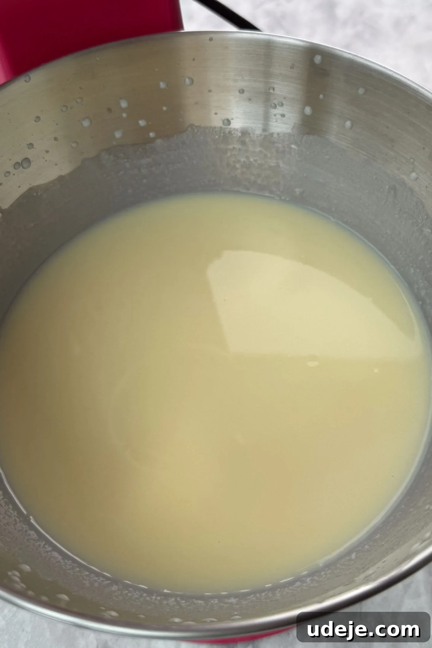 Magnolia Bakery's Irresistible Banana Pudding 5 A light yellow liquid mixture in the silver bowl of a stand mixer on a marble background.