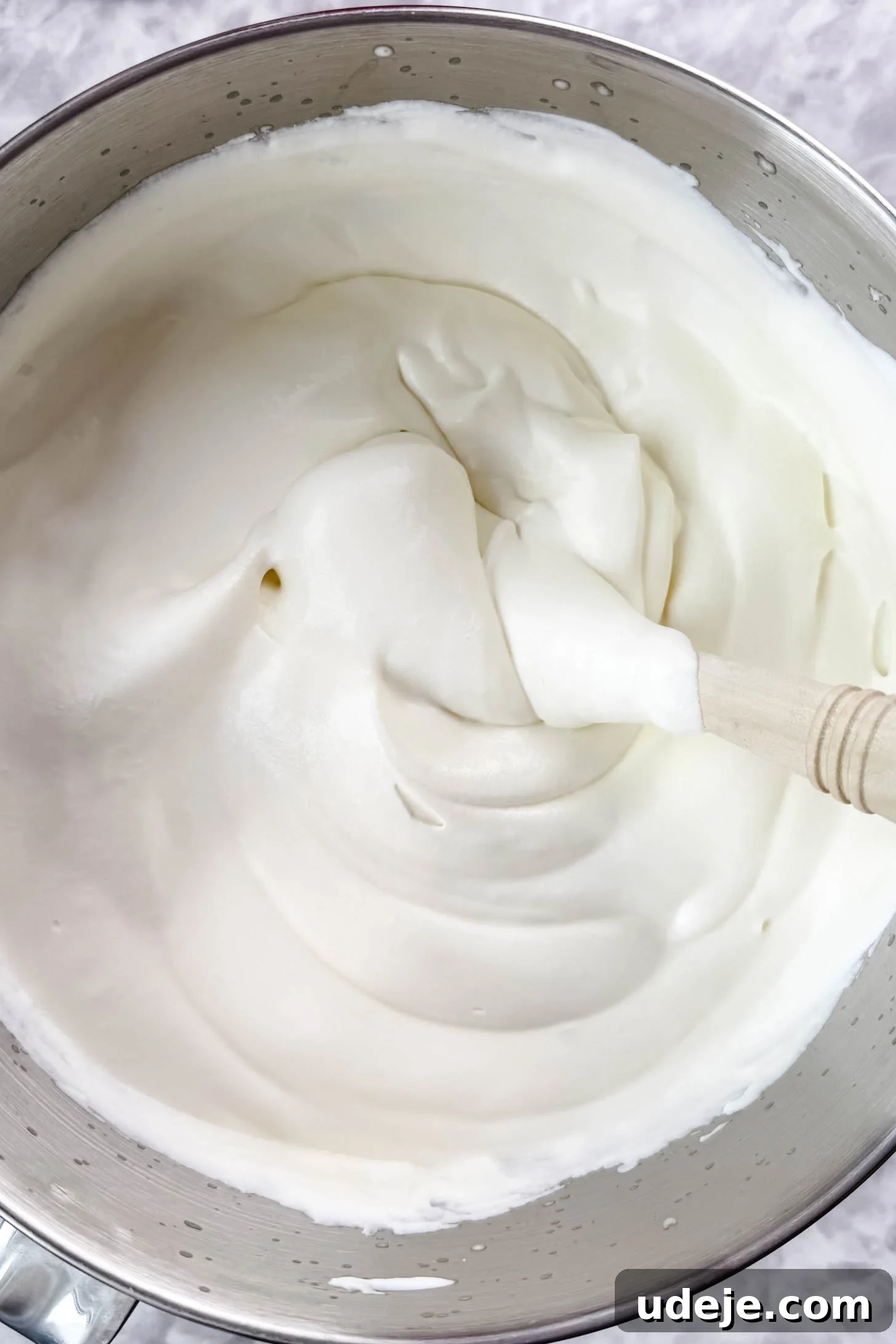 Magnolia Bakery's Irresistible Banana Pudding 9 Cream filling in the silver bowl of a stand mixer with a spatula in it on a marble background.