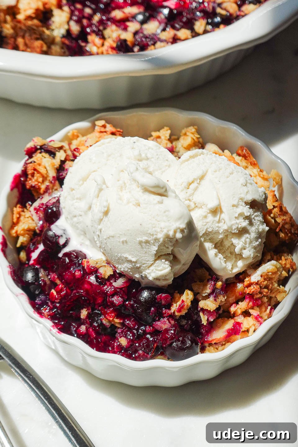 Guilt-Free Blueberry Crisp 2 Healthy blueberry crisp served with a generous scoop of creamy vegan vanilla ice cream, highlighting the golden-brown crisp topping and juicy fruit filling.