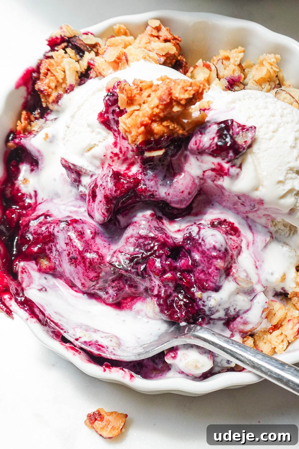 Guilt-Free Blueberry Crisp 5 A close-up of a serving of healthy blueberry crisp, showing the warm, jammy blueberries underneath a perfectly crispy, nutty oat topping, with a melting scoop of vegan vanilla ice cream.
