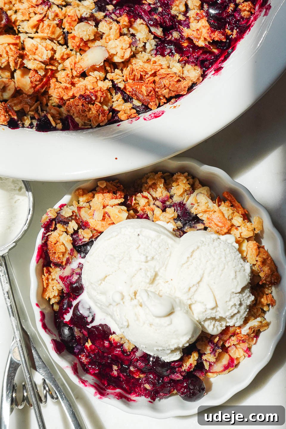 Guilt-Free Blueberry Crisp 8 A top-down shot of a freshly baked healthy blueberry crisp, golden and bubbly, served with a scoop of vegan vanilla ice cream, ready to be enjoyed.